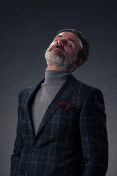 Portrait of a successful stylish elegant senior businessman with a grey beard and casual business clothes confident in photo studio isolated on dark background gesturing with hands. High-quality photo