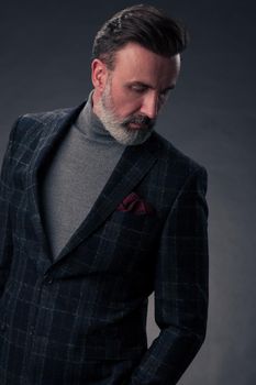 Portrait of a successful stylish elegant senior businessman with a grey beard and casual business clothes confident in photo studio isolated on dark background gesturing with hands. High-quality photo