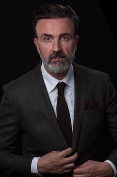 Portrait of a successful stylish elegant senior businessman with a grey beard and casual business clothes confident in photo studio isolated on dark background gesturing with hands. High-quality photo