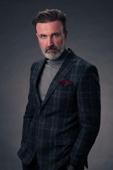 Portrait of a successful stylish elegant senior businessman with a grey beard and casual business clothes confident in photo studio isolated on dark background gesturing with hands. High-quality photo