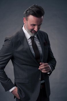 Portrait of a successful stylish elegant senior businessman with a grey beard and casual business clothes confident in photo studio isolated on dark background gesturing with hands. High-quality photo