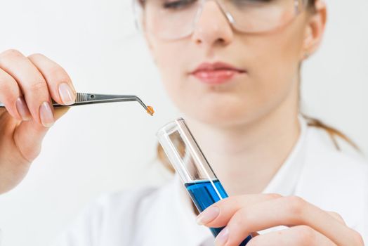 Scientist puts sample into test tube with liquid. Biochemistry laboratory analysis and experimentation. Closeup woman hands holding test tube and tweezers. Biology researching and lab testing.