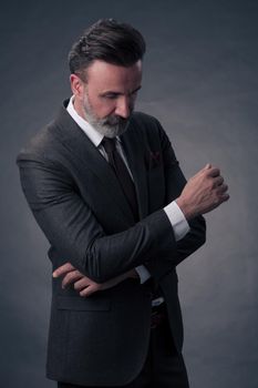 Portrait of a successful stylish elegant senior businessman with a grey beard and casual business clothes confident in photo studio isolated on dark background gesturing with hands. High-quality photo