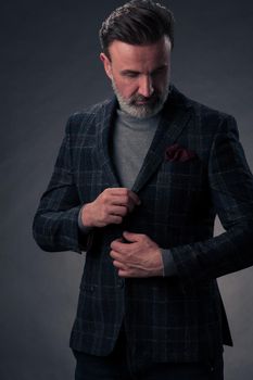 Portrait of a successful stylish elegant senior businessman with a grey beard and casual business clothes confident in photo studio isolated on dark background gesturing with hands. High-quality photo