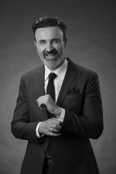 Portrait of a successful stylish elegant senior businessman with a grey beard and casual business clothes confident in photo studio isolated on dark background gesturing with hands. High-quality photo