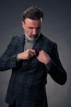 Portrait of a successful stylish elegant senior businessman with a grey beard and casual business clothes confident in photo studio isolated on dark background gesturing with hands. High-quality photo