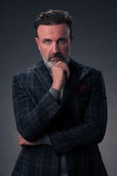 Portrait of a successful stylish elegant senior businessman with a grey beard and casual business clothes confident in photo studio isolated on dark background gesturing with hands. High-quality photo