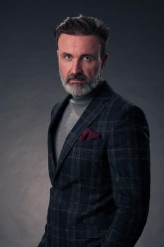 Portrait of a successful stylish elegant senior businessman with a grey beard and casual business clothes confident in photo studio isolated on dark background gesturing with hands. High-quality photo