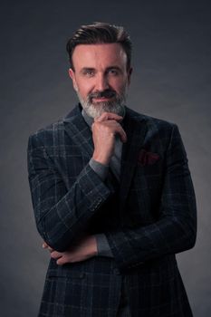 Portrait of a successful stylish elegant senior businessman with a grey beard and casual business clothes confident in photo studio isolated on dark background gesturing with hands. High-quality photo