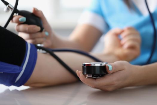 Close-up of doctor measuring patients blood pressure with tonometer tool on planned appointment. Health checkup at family doctor. Medicine, help concept