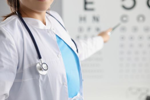 Close-up of female eye doctor point on letter on eye test chart. Optician in uniform, appointment in eye clinic. Checkup, health, ophthalmologist concept