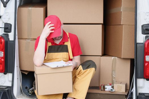 Close-up of delivery man sit in van with delivery receipt and wait for client. Middle aged courier in red uniform. Fast shipping, address delivery concept