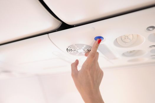 Close-up of airplane passenger female press blue button on plane with finger, stewardess call panel. Flight attendant call knob. Aircraft, service concept