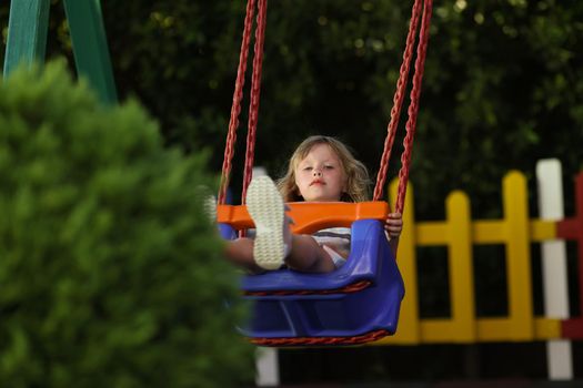 Portrait of little girl having fun on swing on playground in park alone. Pretty kid enjoy ride outdoors, place for children. Childhood, nature, joy concept