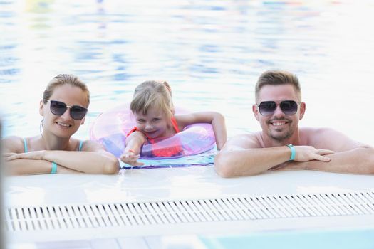 Portrait of happy family posing for picture together in swimming pool. Memorable vacation in luxury resort, family holiday. Summer, childhood, trip concept