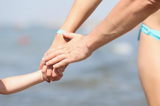 Close-up of family holding hands, mother father and child walking on coastline. Cropped picture of warm and lovable relationships in family. Love concept