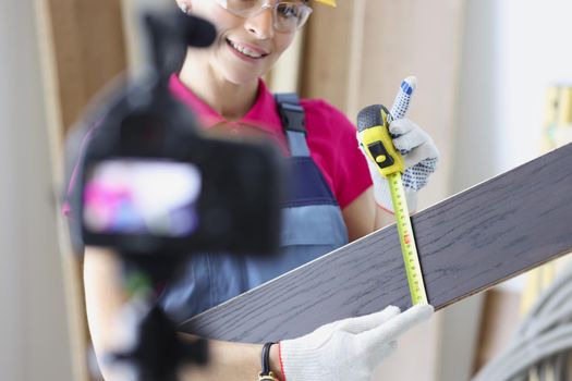 Portrait of smiling woman construction site worker measure plank with tape measure tool. Woman film educational lesson. Renovation, social media concept