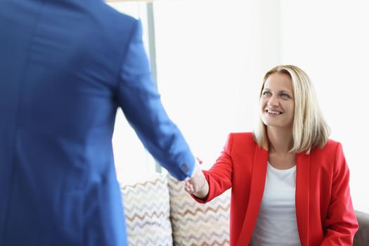 Portrait of cheerful blonde young lady greeting man with handshake sitting on sofa. Business meeting to discuss agreement. Deal, lunch time, career concept