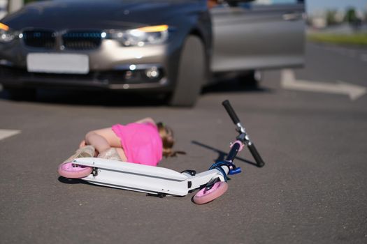Close-up of little girl with scooter hit on road by automobile, road accident. Car driver didnt notice child on highway. Accident, violation, stop concept