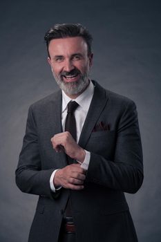 Portrait of a successful stylish elegant senior businessman with a grey beard and casual business clothes confident in photo studio isolated on dark background gesturing with hands. High-quality photo