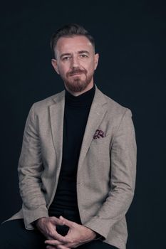 Portrait of adult businessman wearing trendy suit and sitting in modern studio on stylish chair against the black background. Horizontal mockup. High quality photo