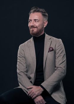 Portrait of adult businessman wearing trendy suit and sitting in modern studio on stylish chair against the black background. Horizontal mockup. High quality photo