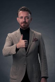 Portrait of a successful stylish elegant senior businessman with a grey beard and casual business clothes confident in photo studio isolated on dark background gesturing with hands. High-quality photo