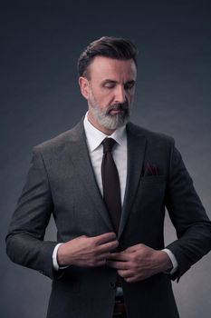 Portrait of a successful stylish elegant senior businessman with a grey beard and casual business clothes confident in photo studio isolated on dark background gesturing with hands. High-quality photo