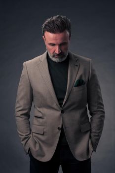 Portrait of a successful stylish elegant senior businessman with a grey beard and casual business clothes confident in photo studio isolated on dark background gesturing with hands. High-quality photo