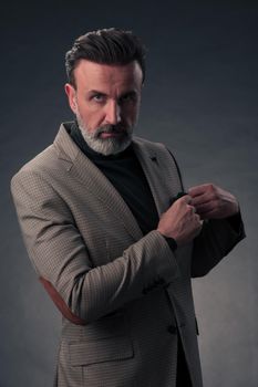 Portrait of a successful stylish elegant senior businessman with a grey beard and casual business clothes confident in photo studio isolated on dark background gesturing with hands. High-quality photo