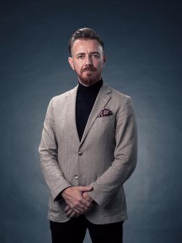 Portrait of a successful stylish elegant senior businessman with a grey beard and casual business clothes confident in photo studio isolated on dark background gesturing with hands. High-quality photo