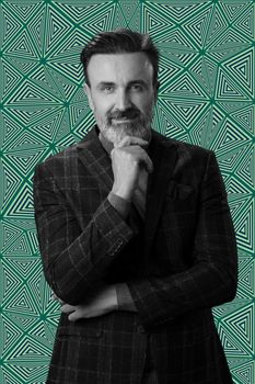 Black and white portrait of a stylish elegant senior businessman with a beard and casual business clothes against retro colorful pattern design background gesturing with hands. High quality photo