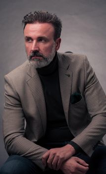 Portrait of a successful stylish elegant senior businessman with a grey beard and casual business clothes confident in photo studio isolated on dark background gesturing with hands. High-quality photo