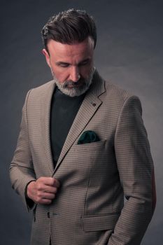 Portrait of a successful stylish elegant senior businessman with a grey beard and casual business clothes confident in photo studio isolated on dark background gesturing with hands. High-quality photo