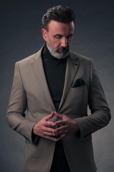 Portrait of a successful stylish elegant senior businessman with a grey beard and casual business clothes confident in photo studio isolated on dark background gesturing with hands. High-quality photo