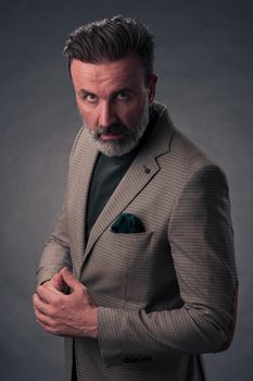 Portrait of a successful stylish elegant senior businessman with a grey beard and casual business clothes confident in photo studio isolated on dark background gesturing with hands. High-quality photo