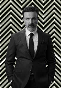 Black and white portrait of a stylish elegant senior businessman with a beard and casual business clothes against retro colorful pattern design background gesturing with hands. High quality photo