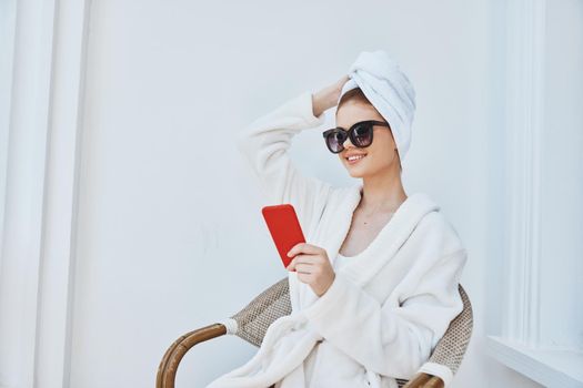 cheerful woman uses a red phone in a chair in a white robe. High quality photo