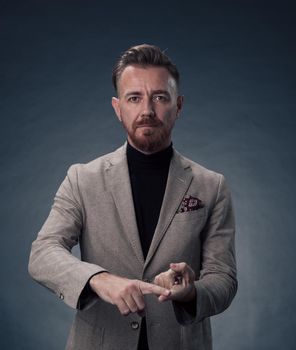 Portrait of a successful stylish elegant senior businessman with a grey beard and casual business clothes confident in photo studio isolated on dark background gesturing with hands. High-quality photo