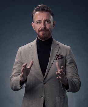 Portrait of a successful stylish elegant senior businessman with a grey beard and casual business clothes confident in photo studio isolated on dark background gesturing with hands. High-quality photo