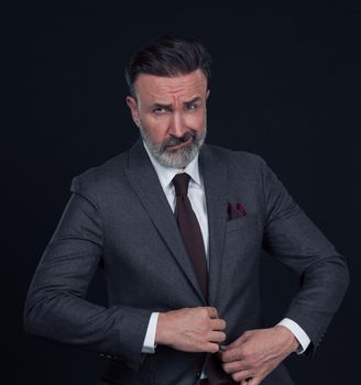 Portrait of a successful stylish elegant senior businessman with a grey beard and casual business clothes confident in photo studio isolated on dark background gesturing with hands. High-quality photo