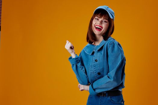 Pretty young female in a cap and denim jacket posing yellow background unaltered. High quality photo