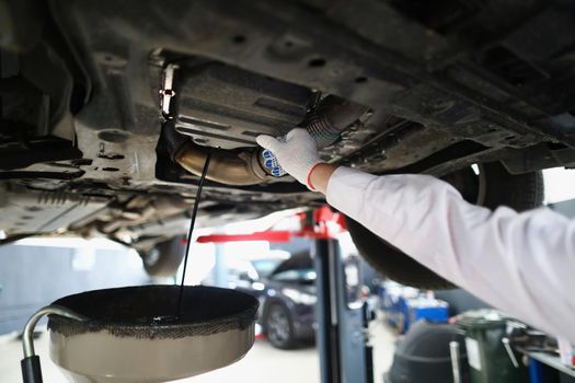 Close-up of mechanic man on car maintenance service change oil under transport. Garage with professional help and workers. Pit stop, fixing service concept