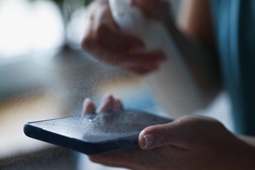 Close-up of spray antiseptic on mobile phone screen, antibacterial and disinfecting liquid. Protective glass on phone screen. Clean, prevent virus concept