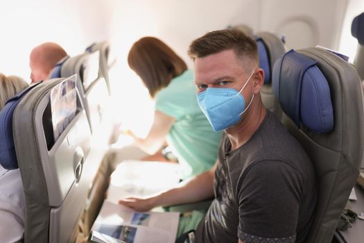 Portrait of couple flying on airplane, reading magazine to kill time. Fly high in sky, wear face masks on flight. Airplane, coronavirus, pandemic concept