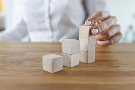 Close-up of female putting wooden brick on top of stack, building tower. Visualizing future plans. Planning, management, strategy, business goal concept