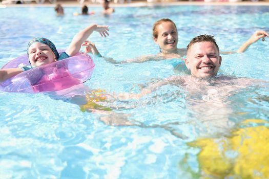 Portrait of mother father and daughter swimming in pool on summer holiday. Happy parent and kid on resort. Summer, childhood, parenthood, leisure concept