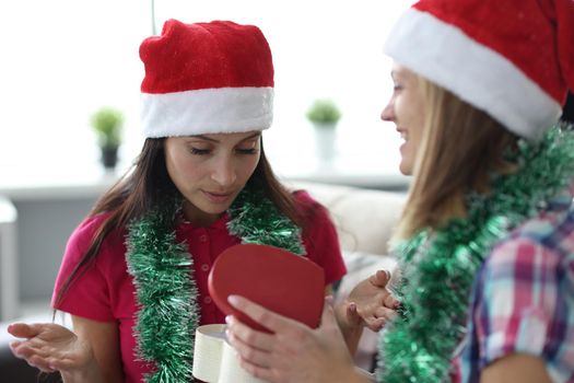Portrait of female in santa claus hat open empty box, no present, practical joke. Female friends exchange gifts every year. Joke, prank, holiday concept
