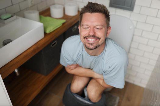 Portrait of man with happy facial expression after toilet, feel better after defecating. Man in bathroom after renovation. Wc, hygiene, nature call concept