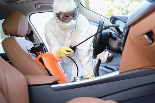 Portrait of hazmat female worker cleanse car interior with spray disinfectant. Disinfect auto upholstery from virus with equipment. Covid prevent concept